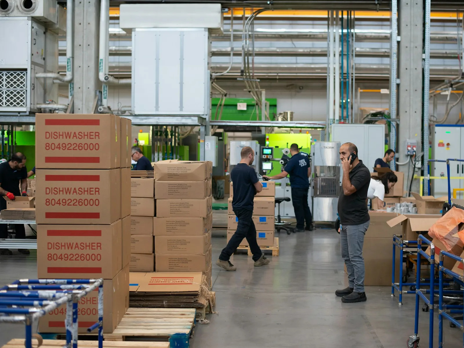 Workers moving stock across a production floor stacked with cartons